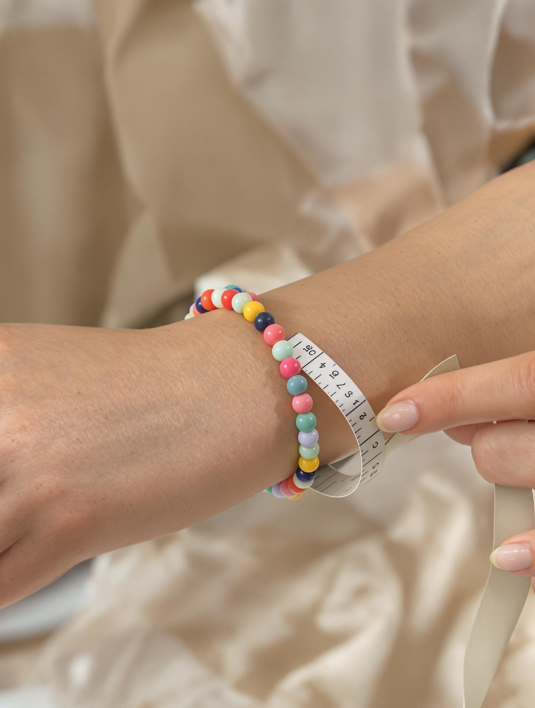 Mesure du poignet avec un mètre ruban pour choisir un bracelet en perles multicolores.
