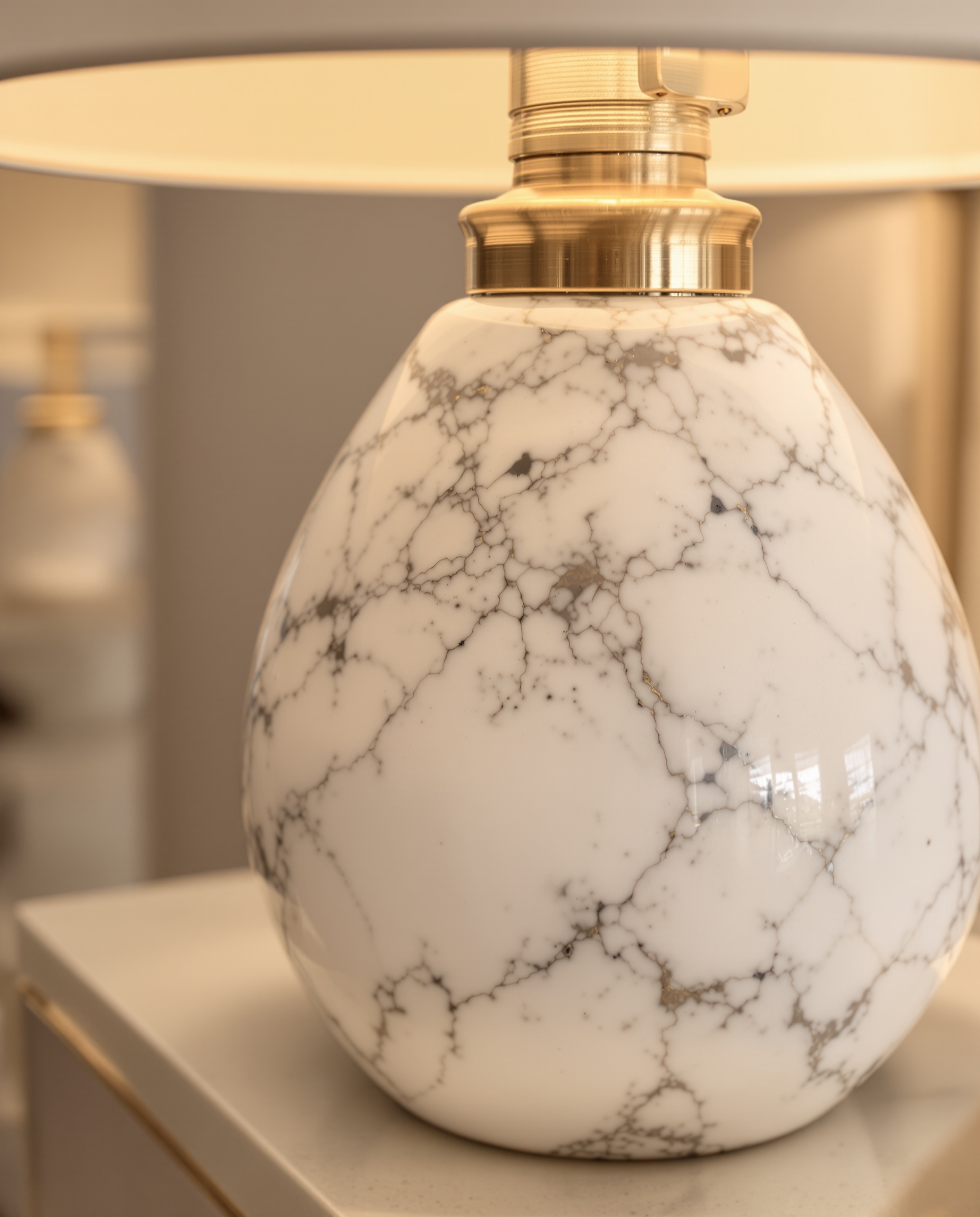 Gros plan sur une lampe de chevet luxe : socle en marbre blanc grain fin, détail brossé en laiton doré, lumière chaude refletant textures impeccables.