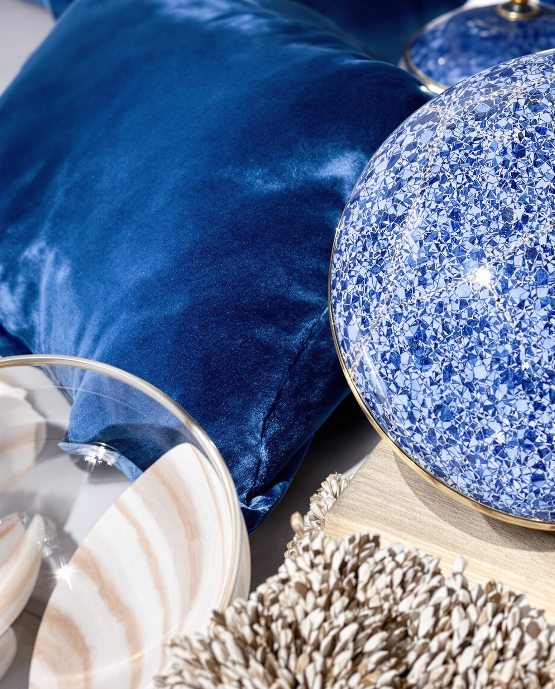 Gros plan sur textures bleu outremer : velours coussin, faïence brillante, bois clair et touche de laiton