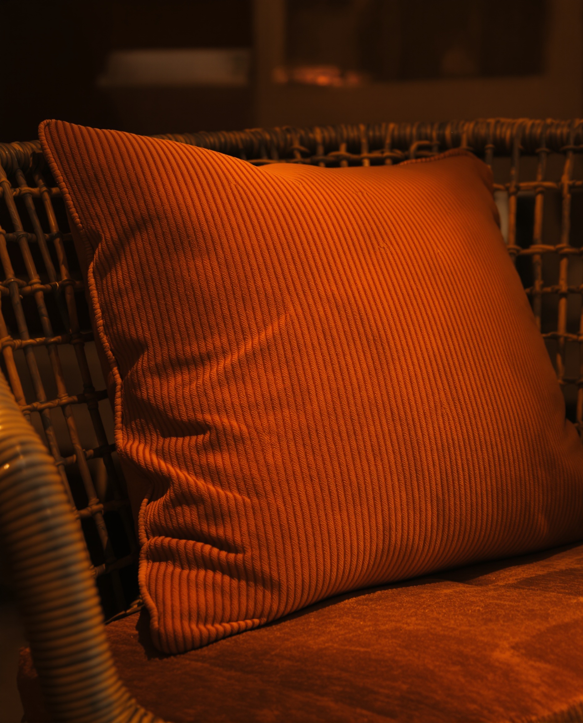 Détail d’un intérieur années 70 mettant en scène velours orange, rotin et plastique fumé