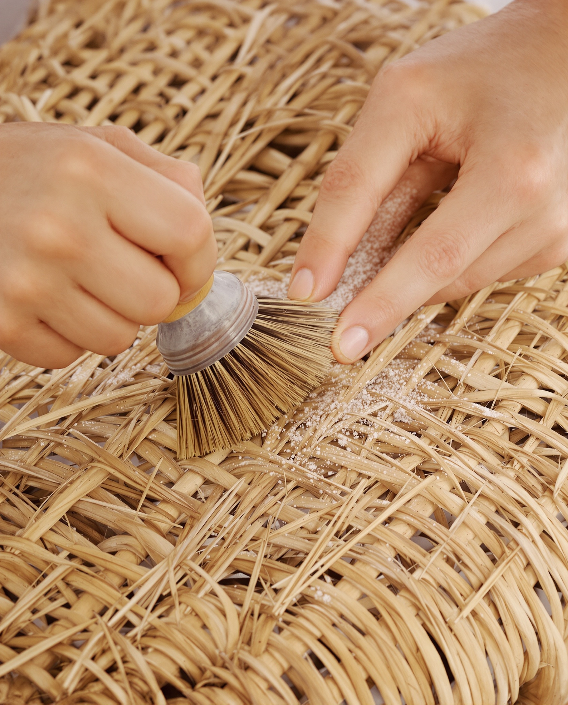 Main nettoyant une assise en paille ancienne avec un petit pinceau