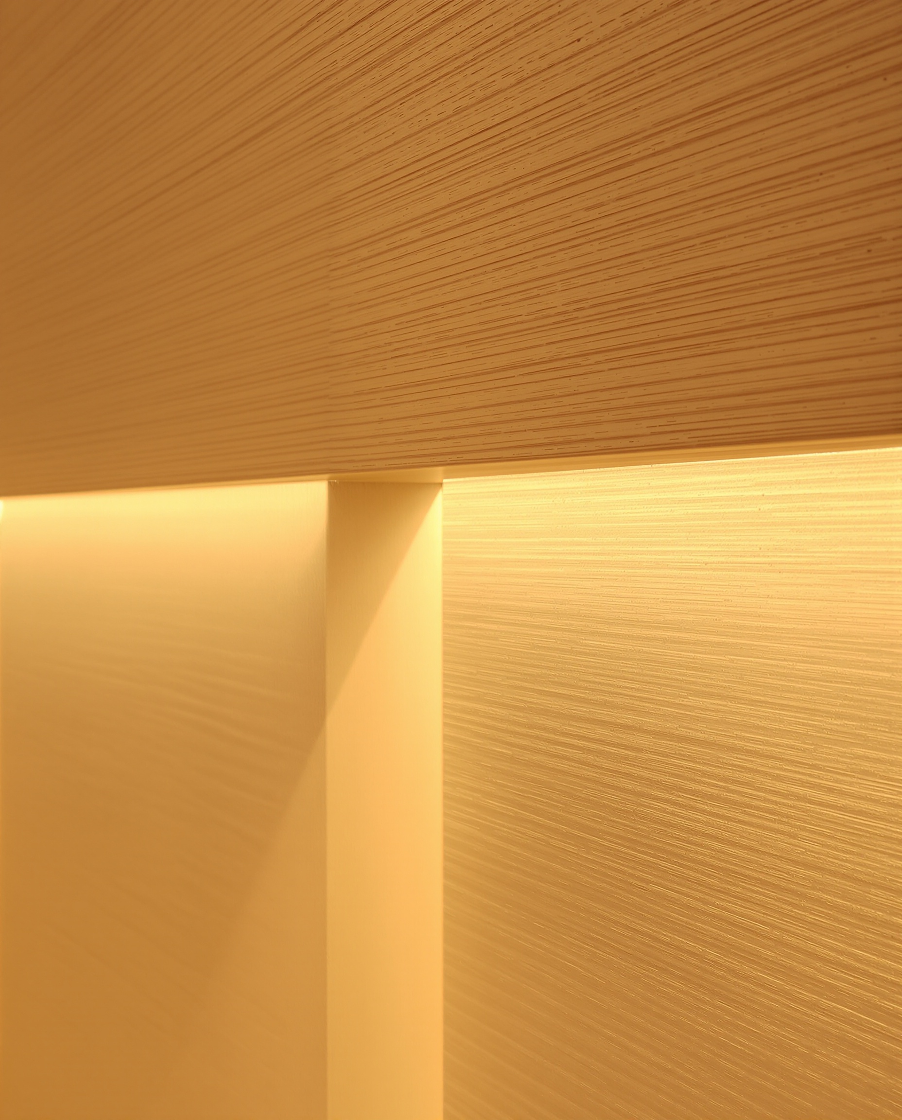 Mur en contreplaqué bouleau, lumière dorée soulignant la texture et les strates visibles.