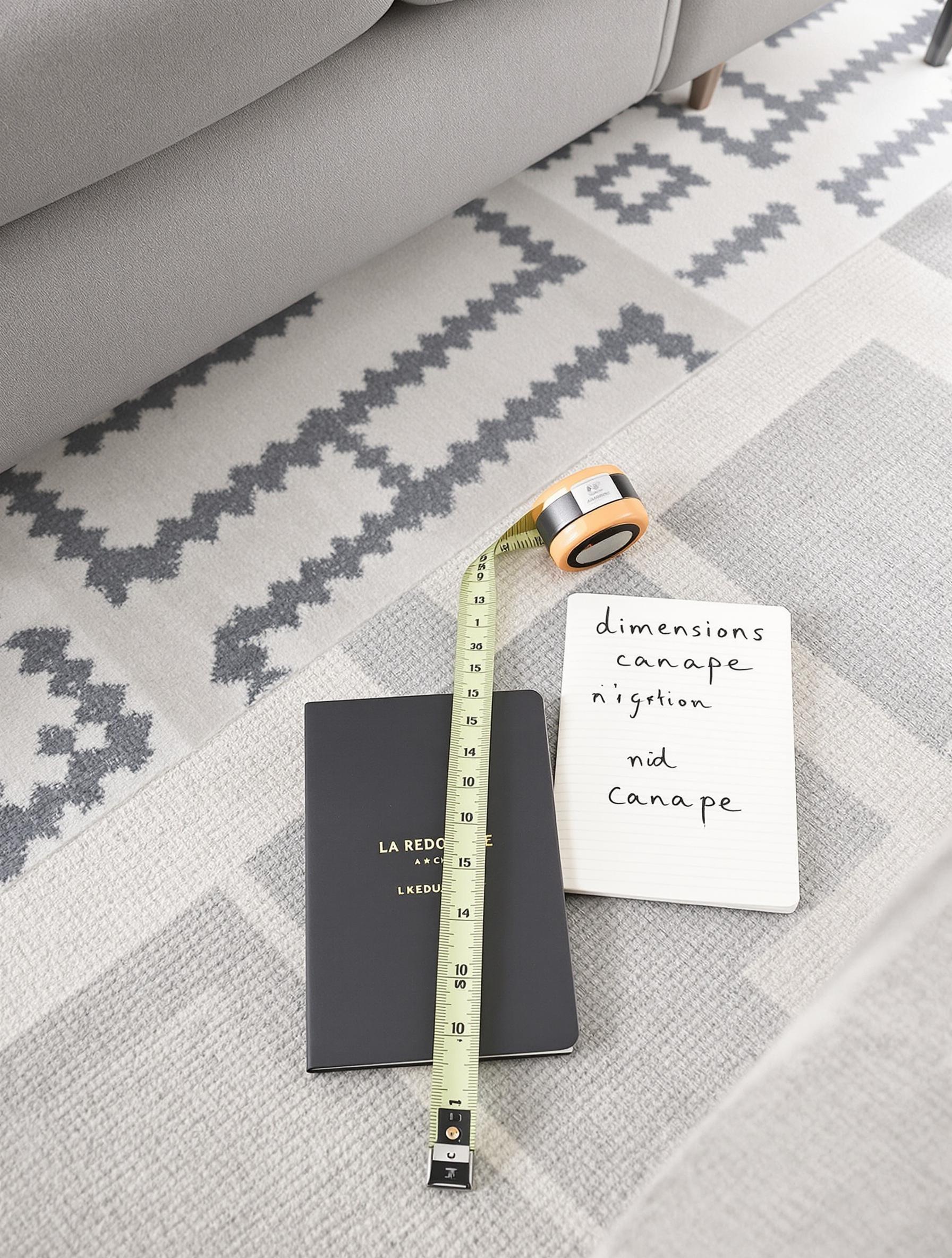 Mètre ruban sur tapis graphique et carnet de dimensions pour canapé