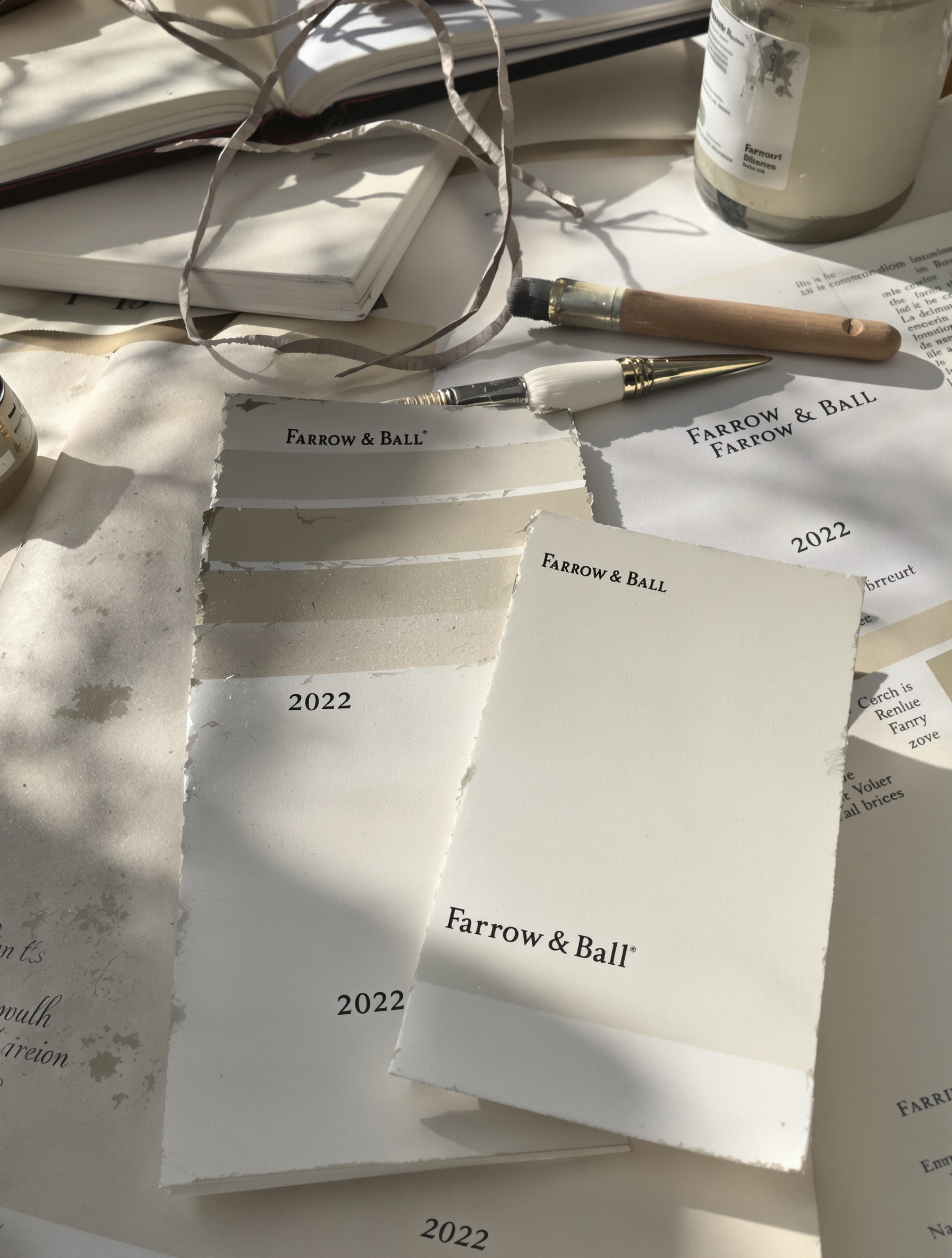 Vieux nuancier Farrow & Ball 2022 corné et taché, à côté d’un nuancier récent sur bureau d’architecte, lumière mélancolique.